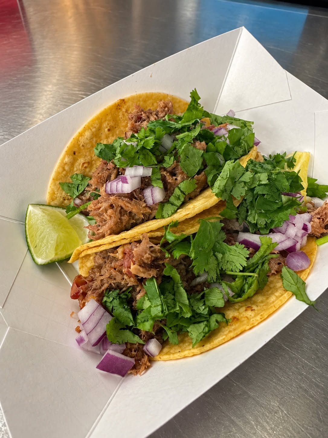 Tacos topped with cilantro and red onion, with lime on the side